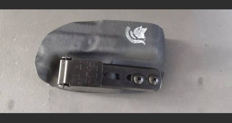May include: Black leather holster with a metal clip and two screws. The holster has a white logo on the top.