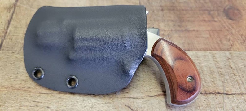 May include: A small, silver revolver with a wooden grip is in a black leather holster. The holster has two metal snaps.
