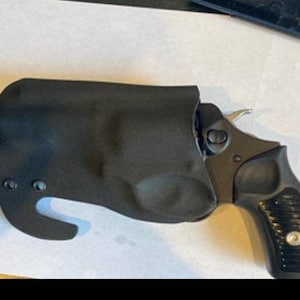 Puede incluir: Una funda de cuero negra con una pistola negra en su interior. La funda tiene un gancho en el lateral y un cierre de presión.