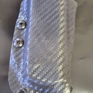 May include: A black carbon fiber magazine holster with two silver screws and a black metal loop.