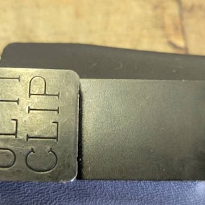 May include: A black leather belt with a metal clip that says "ULTI CLIP" on it. The clip is attached to the belt with a screw.