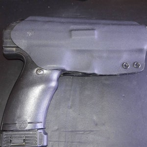 May include: Black handgun with a black holster. The holster has two metal eyelets on the side. The gun has a black grip with a "Hi-Point" logo.