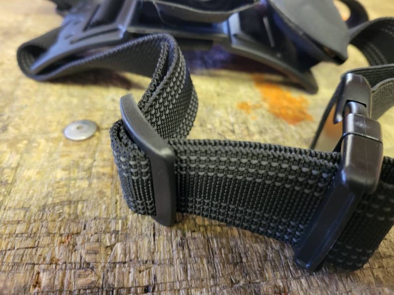 May include: Close-up of a black adjustable strap with a textured fabric and a plastic buckle.