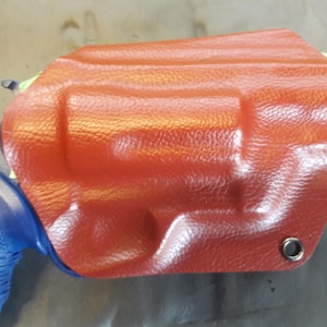 Könnte beinhalten: Ein rotes Lederholster für eine Pistole mit einem Metallösen.