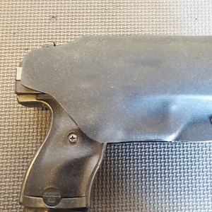 May include: A black leather holster for a handgun. The holster has a textured surface and a small metal screw on the side.