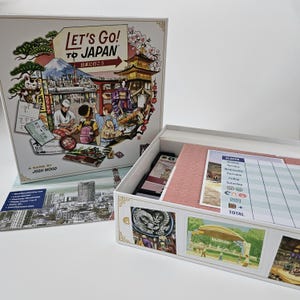 Peut inclure: Un jeu de société intitulé Let's Go! To Japan par Josh Wood, avec un couvercle de boîte illustré de monuments japonais, d'un chat porte-bonheur et de personnages. La boîte ouverte contient une feuille de score avec des colonnes pour les jours.