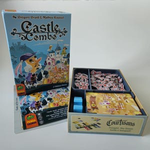 May include: Castle Combo board game box featuring a light blue cover with a cartoon character on a horse and a castle. The open game box contains red key tokens, blue wooden pieces, and a deck of cards with the text Courtisans Tonight the Queen holds a banquet.