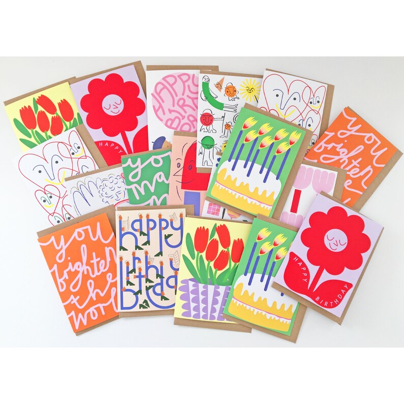 May include: A collection of colorful greeting cards with various designs. The cards feature illustrations of flowers, cakes, and abstract shapes, along with handwritten text such as "Happy Birthday" and "You Brighten the World". The cards have a kraft paper backing.