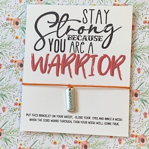 May include: A white card with the words "Stay Strong Because You Are A Warrior" in black and red script. An orange string bracelet with a silver "Warrior" charm is attached. The card includes instructions.