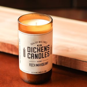 May include: A brown glass candle jar with a white label. The label says "100% Soy Wax Candle", "Dickens Candles", "Scent: Rich Mahogany", and "DickensCandles.com".
