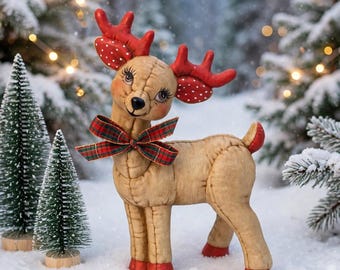 May include: A tan fabric reindeer figurine with red antlers featuring white polka dots, long eyelashes, and a red and green plaid ribbon tied around its neck. The reindeer has red hooves and a small red tail, standing in a snowy outdoor setting.