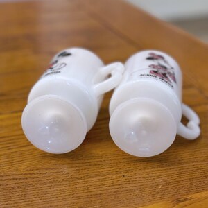 K&ouml;nnte beinhalten: Zwei wei&szlig;e Glasbecher mit ausgestelltem Boden und Henkel. Jeder Becher zeigt eine Minnie Mouse-Grafik in Schwarz, Rot und Rosa. Die Becher stehen auf einer Holzoberfl&auml;che.