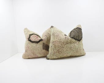 May include: Three textured throw pillows. The pillows have a light beige background with dark brown and pink geometric designs. The pillows are arranged on a white surface, creating a neutral and cozy aesthetic.