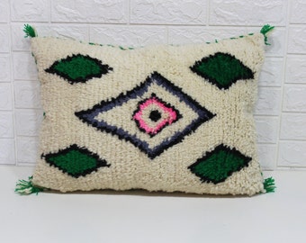 May include: A white throw pillow with a geometric pattern in shades of green, black, pink, and gray. The pillow has tassels on the corners.