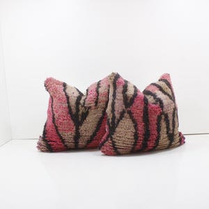 Puede incluir: Dos cojines decorativos con un diseño texturizado y estampado. Los cojines presentan una combinación de colores rosa, marrón y negro. El patrón parece ser una serie de rayas o líneas verticales.