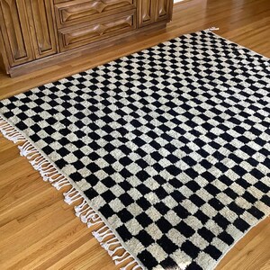 May include: Black and white checkered rug with fringe. The rug has a woven texture and is made of wool.