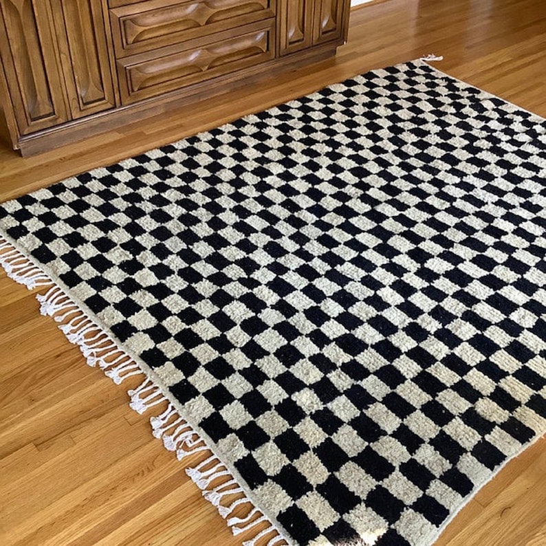 May include: Black and white checkered rug with fringe. The rug has a woven texture and is made of wool.