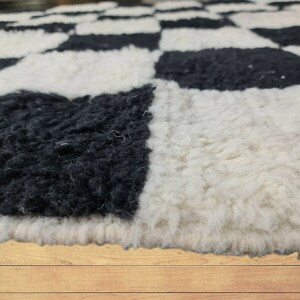 May include: Close-up of a black and white checkered rug made of fluffy, soft material. The rug is made of wool and has a textured surface. The rug is on a wooden floor.