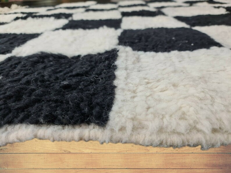 May include: Close-up of a black and white checkered rug made of fluffy, soft material. The rug is made of wool and has a textured surface. The rug is on a wooden floor.