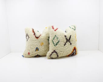 May include: Two off-white, textured throw pillows with colorful geometric designs. The pillows feature red, green, yellow, and brown patterns, creating a cozy and decorative accent for any living space.
