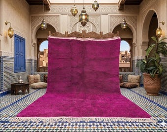May include: A large, vibrant magenta rug with a thick pile and a white fringe. The rug is displayed in a room with ornate architectural details, including arches, carved wood, and decorative tilework. The room is lit by hanging lanterns.
