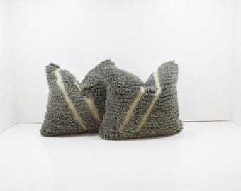 May include: Two gray textured throw pillows with a diagonal cream-colored stripe. The pillows have a soft, shaggy appearance and are arranged against a white background. The pillows are a decorative home accent.