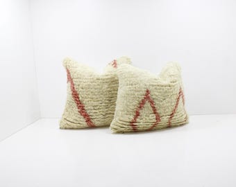 May include: Two square, textured throw pillows. The pillows are off-white with a red geometric pattern. The pillows are placed on a white surface and are suitable for home decor.