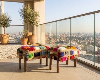 May include: Two rectangular ottomans featuring a textured, multi-colored tufted fabric top in shades of red, blue, yellow, green, and white, supported by four dark brown wooden legs. The ottomans have a woven base and a plush, shaggy surface.
