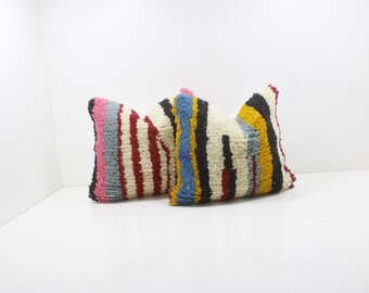 May include: Two decorative throw pillows with a textured, striped design. One pillow features vertical stripes in red, white, and pink. The other pillow has stripes in black, blue, yellow, and red. These pillows add a pop of color and texture to any room.