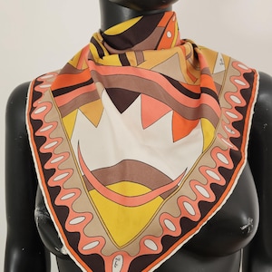 May include: A square silk scarf featuring a geometric pattern in shades of orange, yellow, brown, and cream. The design includes a border with repeating oval shapes and abstract triangular and curved motifs throughout the center of the fabric.