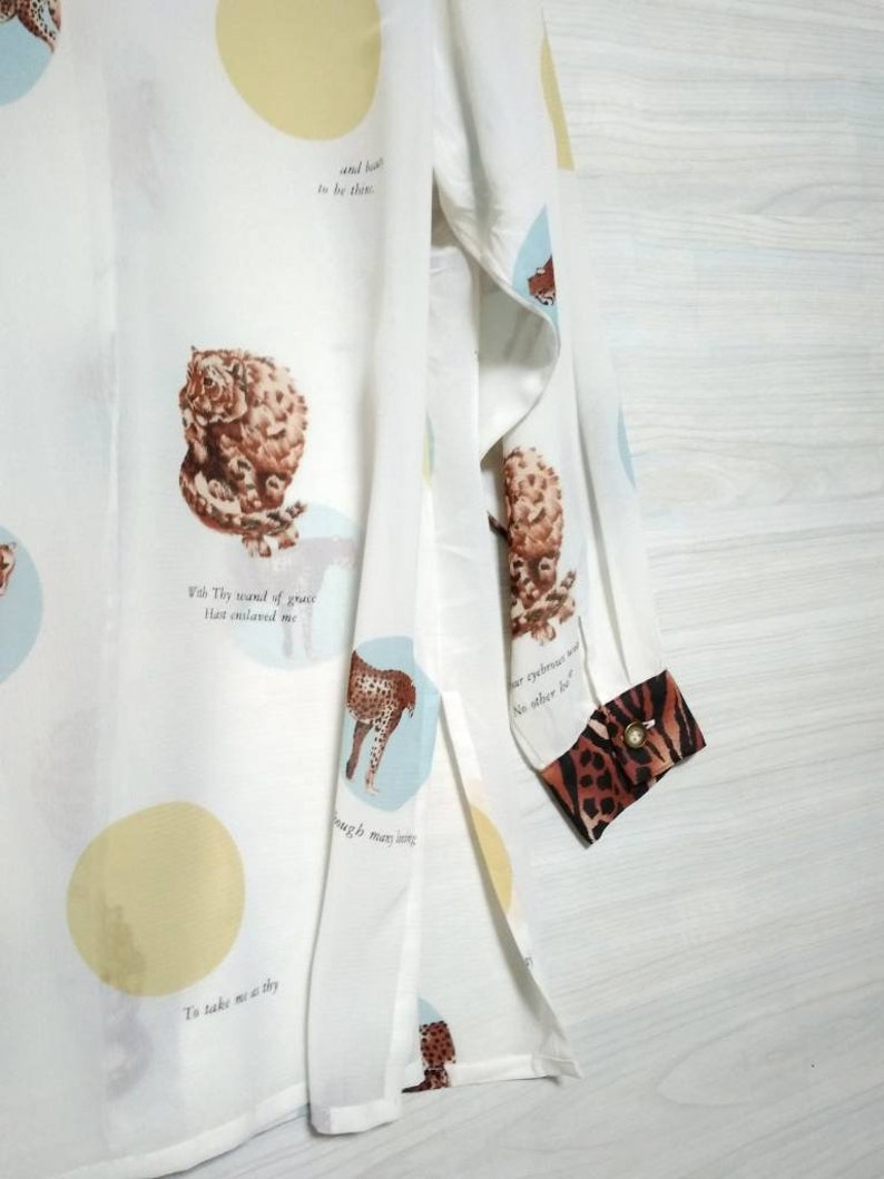 May include: White long-sleeved shirt with a print of various animals and text. The text includes "With Thy wound of grace That enlaved me" and "To take me as thy". The shirt has a leopard print cuff.