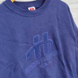 Pode incluir: Uma camisola azul marinho com um grande logotipo bordado que diz "NORTH CAROLINA U.S.A."