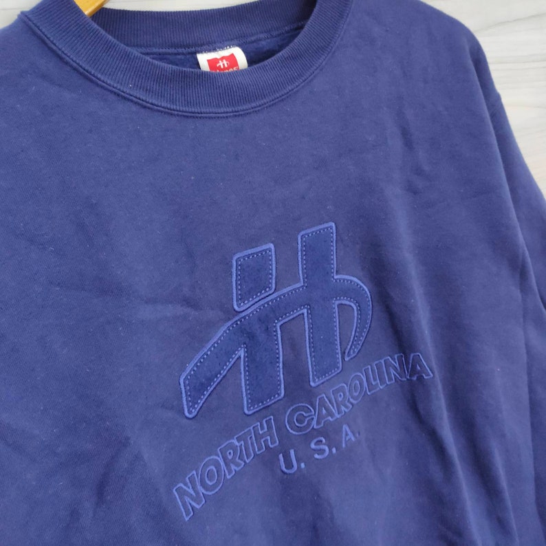 Pode incluir: Uma camisola azul marinho com um grande logotipo bordado que diz "NORTH CAROLINA U.S.A."
