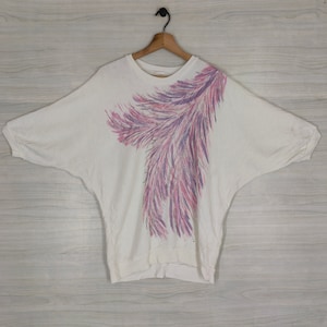 May include: White oversized t-shirt with a pink and purple abstract feather design.