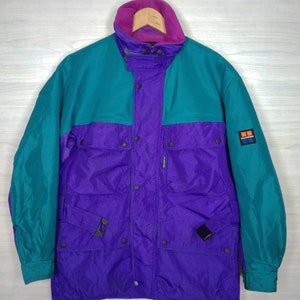 Peut inclure: Une veste de ski vintage turquoise, violette et rose avec une doublure en polaire et plusieurs poches. La veste a une fermeture à pression et un écusson de marque sur la manche qui indique "High Sierra".