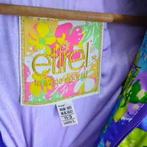 May include: A purple jacket with a floral print and a purple zipper. The jacket has a label that says "etirele le style sportif" and has the size information "Bust 85, Length 160, 11-3, Ladies' L".