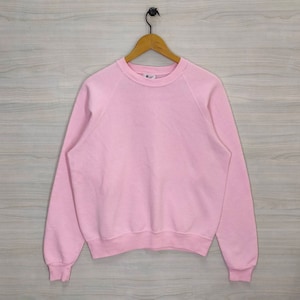 May include: A pink crew neck sweatshirt with long sleeves and a ribbed hem.
