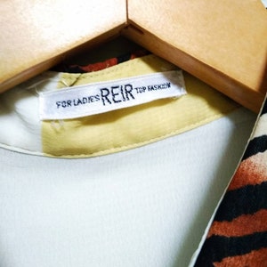 May include: A white tag with black text that reads "FOR LADIES REIR TOP FASHON" on a yellow background. The tag is attached to a light blue shirt with a brown and black zebra print.