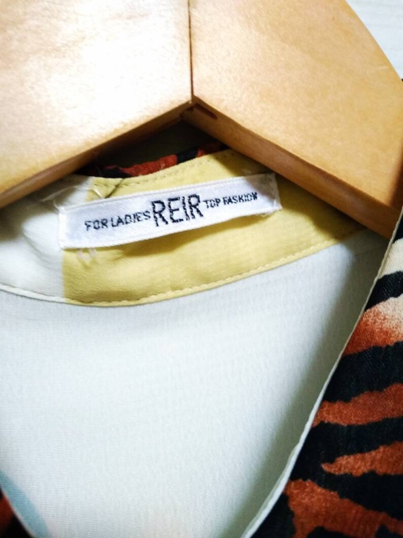 May include: A white tag with black text that reads "FOR LADIES REIR TOP FASHON" on a yellow background. The tag is attached to a light blue shirt with a brown and black zebra print.
