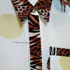 May include: White button-up shirt with a tiger print collar and trim. The shirt has a pocket on the left side and features a cheetah print design with the text "To take me as thy".