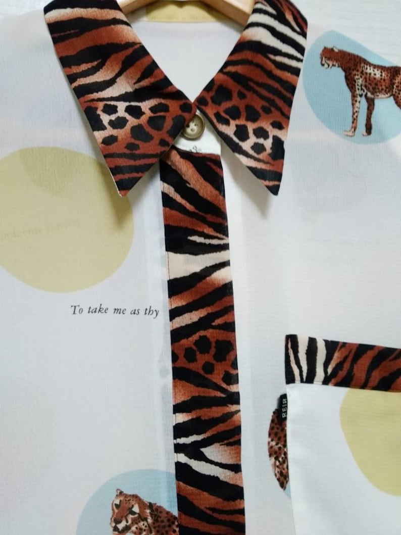 May include: White button-up shirt with a tiger print collar and trim. The shirt has a pocket on the left side and features a cheetah print design with the text "To take me as thy".