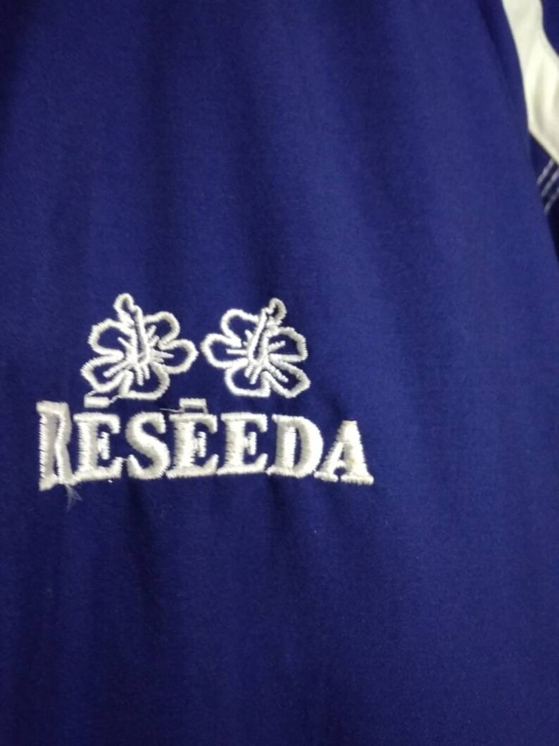 May include: A blue jacket with white embroidered flowers and the word "RESEEDA" on the front.