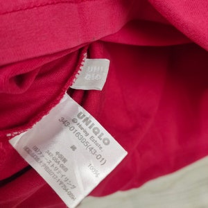 May include: White tag with black text on a red fabric background. The tag reads "UNIQLO Haring Estate. 343-016395(43-01) 綿 100% 中国製 342-05A-068 (株)ファーストリテイリング 山口県山口市大字佐山717-1〒754-0894".