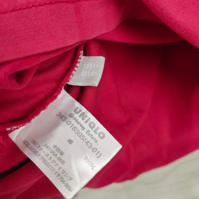 May include: White tag with black text on a red fabric background. The tag reads "UNIQLO Haring Estate. 343-016395(43-01) 綿 100% 中国製 342-05A-068 (株)ファーストリテイリング 山口県山口市大字佐山717-1〒754-0894".