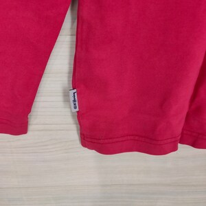 May include: A long-sleeved, pink t-shirt with a small white tag that says "@K-Heine".