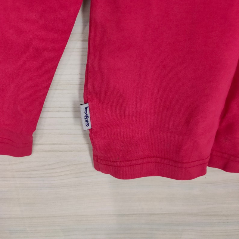 May include: A long-sleeved, pink t-shirt with a small white tag that says "@K-Heine".