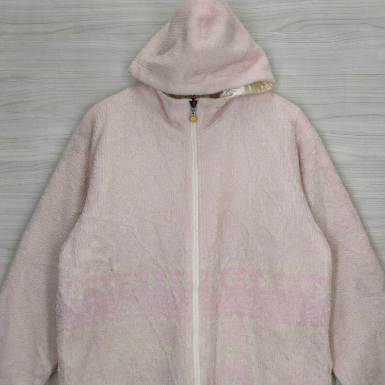 May include: A pink fleece zip-up jacket with a hood. The jacket has a white zipper and a white pattern on the front.