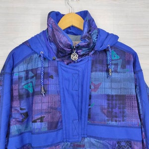 Puede incluir: Una chaqueta azul con capucha con un patr&oacute;n geom&eacute;trico en tonos de morado, azul y verde. La chaqueta tiene una cremallera y una capucha con cord&oacute;n.