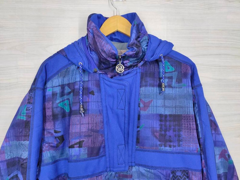 Puede incluir: Una chaqueta azul con capucha con un patr&oacute;n geom&eacute;trico en tonos de morado, azul y verde. La chaqueta tiene una cremallera y una capucha con cord&oacute;n.
