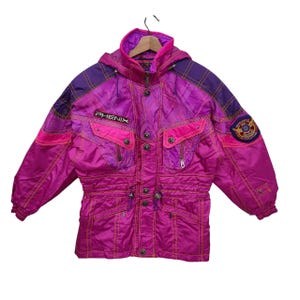 Könnte beinhalten: Eine Vintage-Skijacke in Magenta und Lila mit Kapuze. Die Jacke hat mehrere Taschen, einen Kordelzug in der Taille und den Markennamen "PHENIX" auf der Brust. Gelbe Nähte akzentuieren das Design. Ein Aufnäher ist auf dem Ärmel sichtbar.
